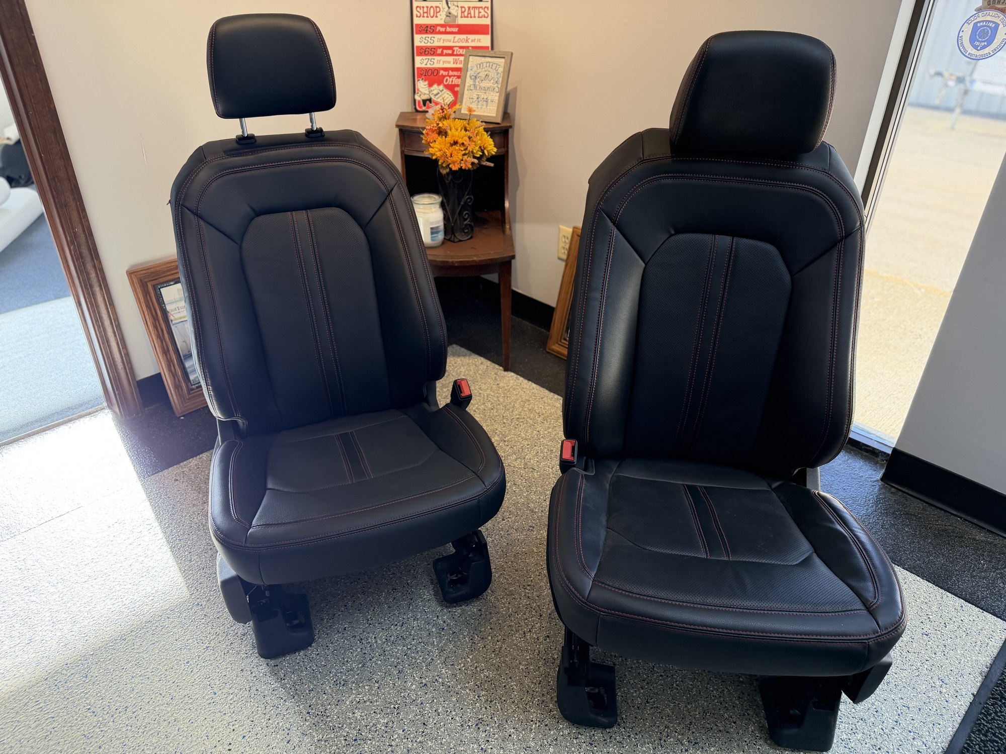 A freshly upholstered pair of black automotive seats with red stitching